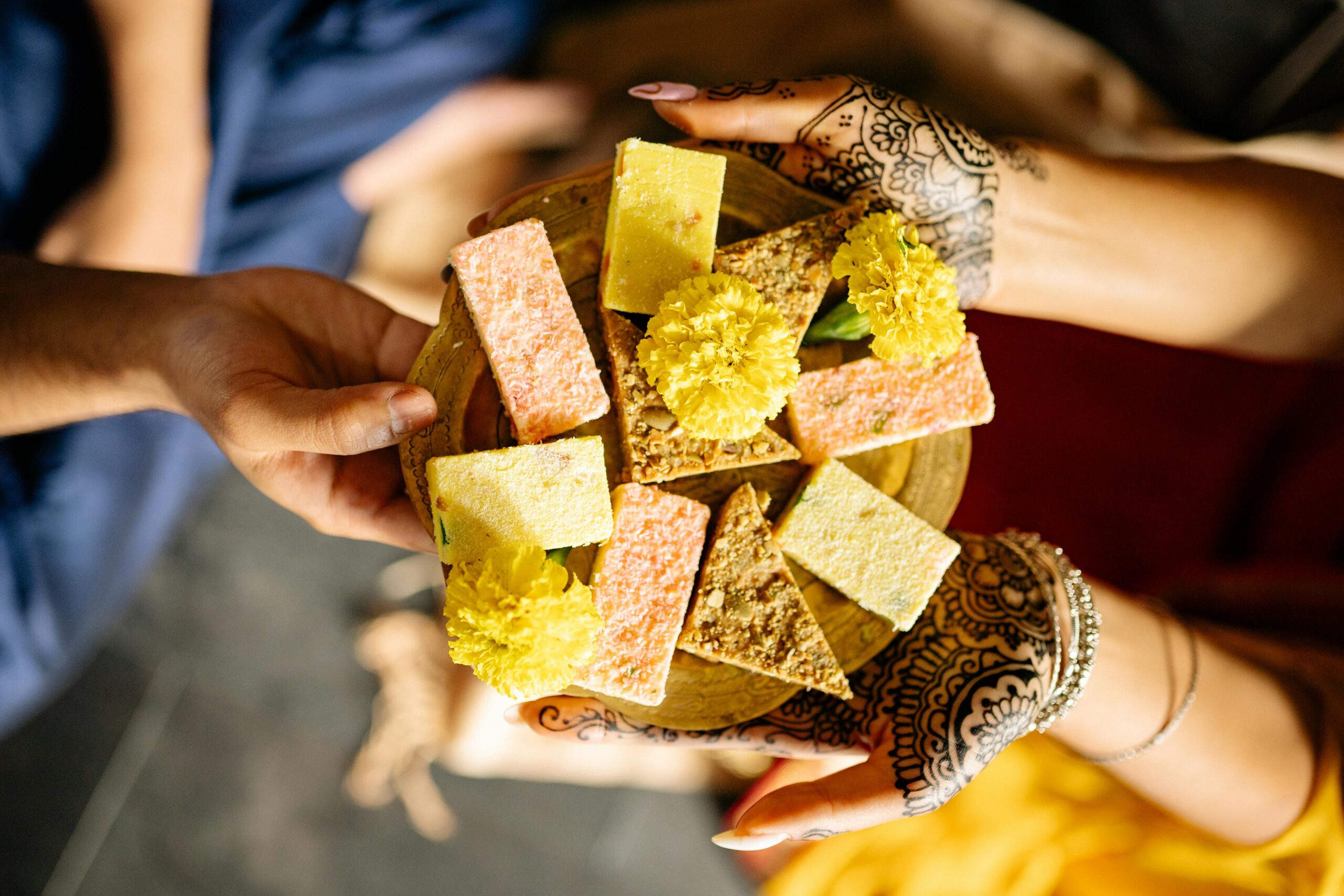 Close-up of hands exchanging a plate of Indian sweets and flowers during Diwali, showcasing cultural richness.
